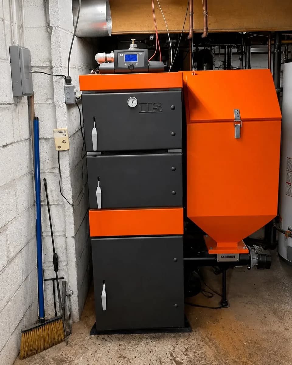 An MBTEK boiler system with a black and orange cabinet unit and an orange hopper, photographed in a utility basement setting.
