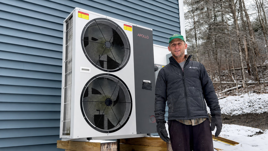 Installer standing beside an Apollo 6 ton air to water heat pump installed outdoors in winter.
