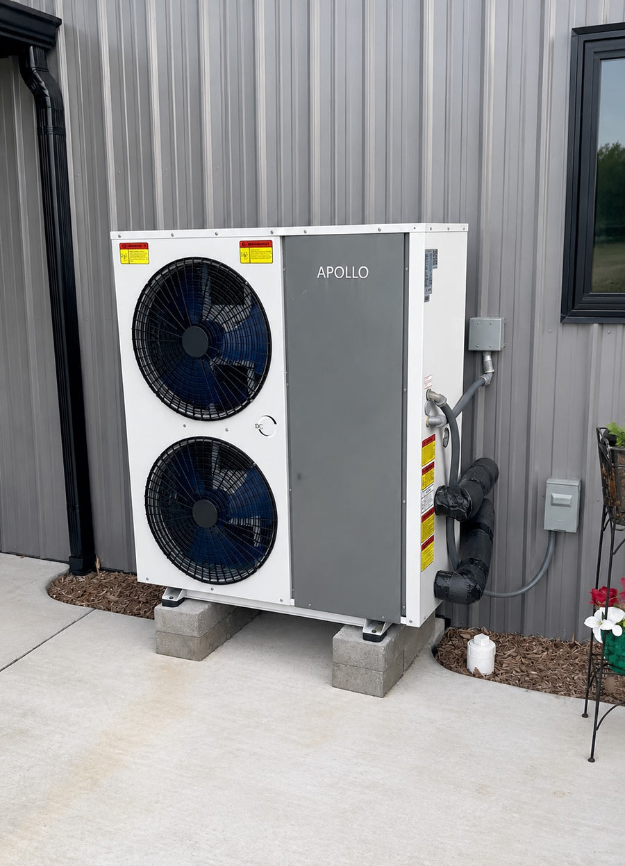 Apollo air to water heat pump installed outdoors on raised concrete blocks beside a metal-sided building.