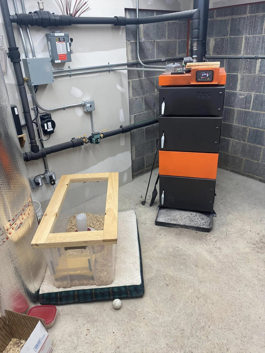 UNI wood boiler installed with insulated hydronic piping beside a clear bin holding wood fuel.